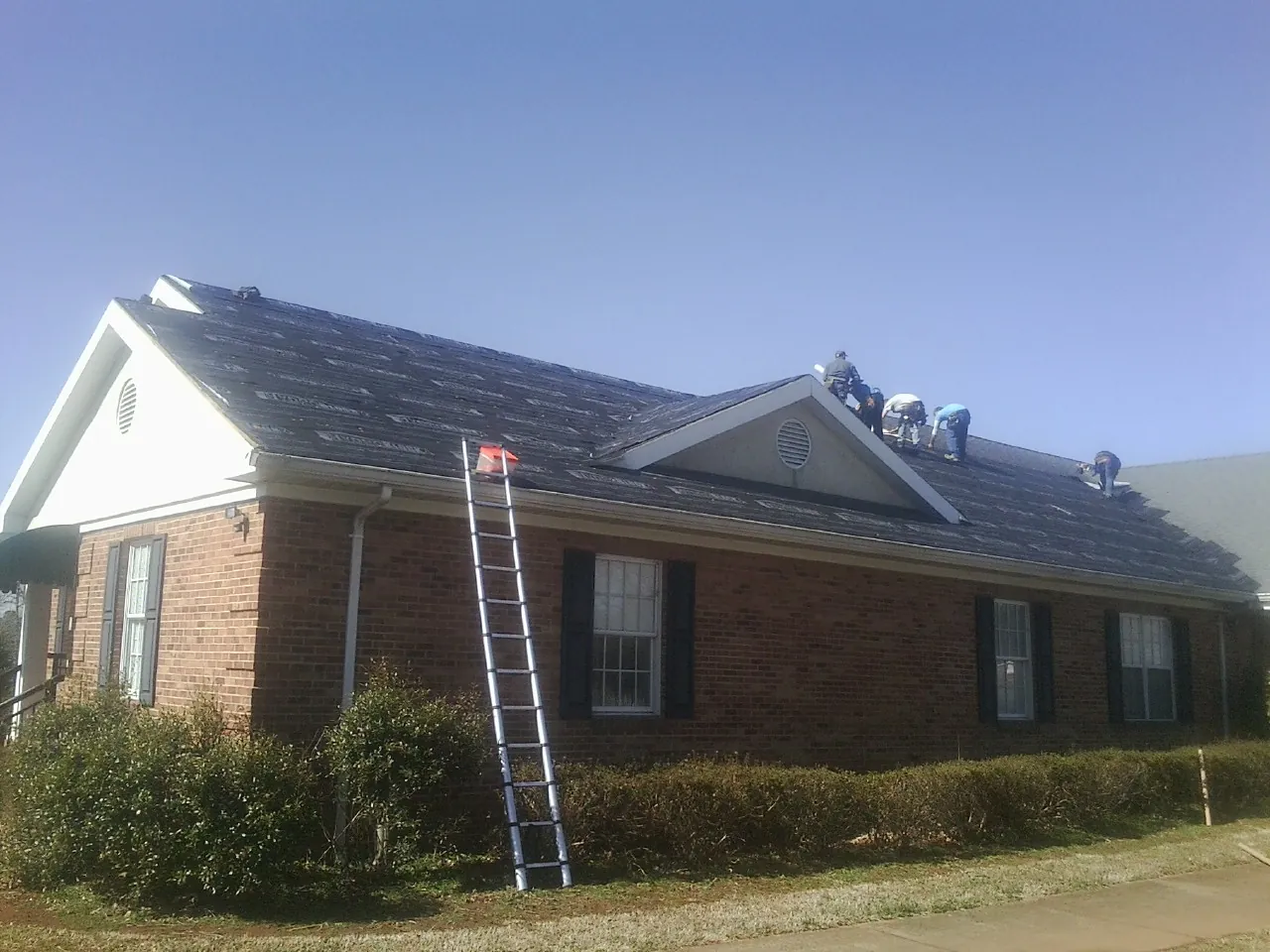 Crew tearing shingles off a brick ranch roof with a ladder set — Metal Roof Repair work by our crew in Wellston