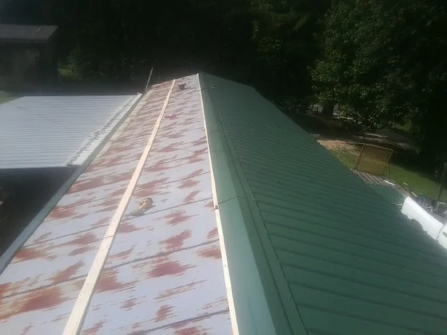 Old rusted panels beside newly installed green metal roofing — Wind Damage Roof Repair by Roofing Brothers in Wellston