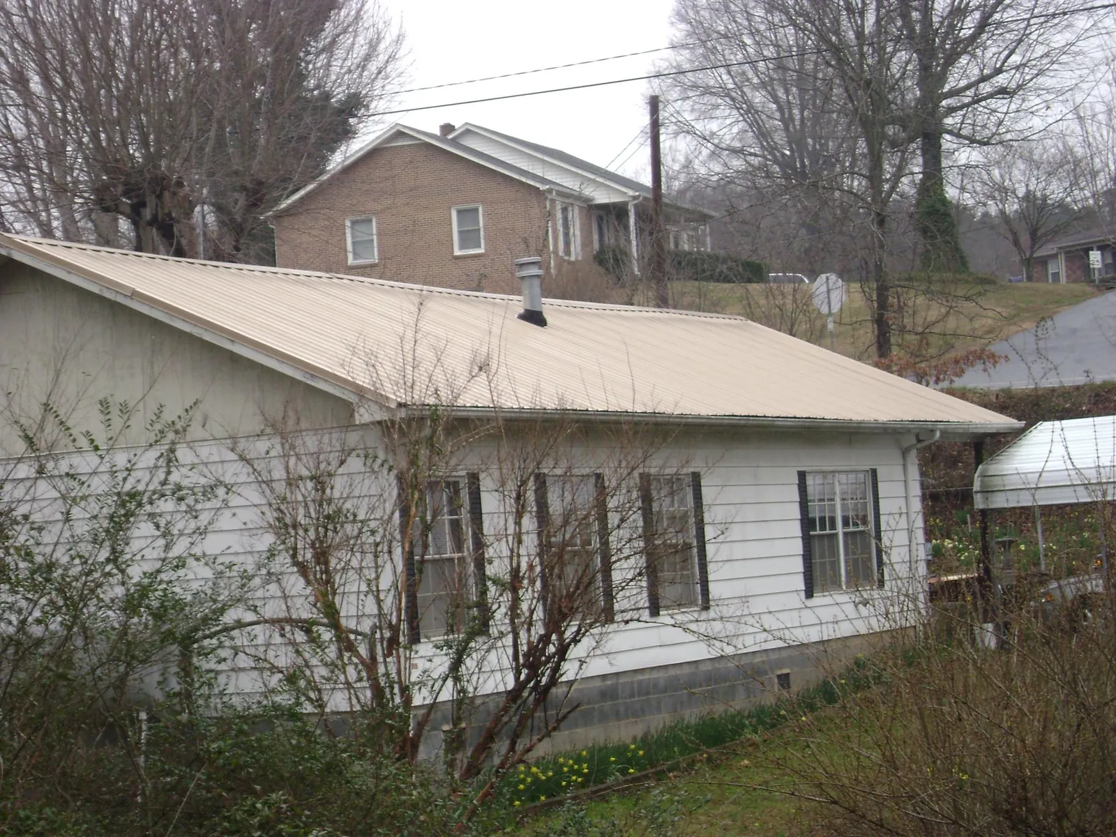 Tan metal roof on a white sided house set into a hillside — Commercial Roofing by Roofing Brothers in Wellston